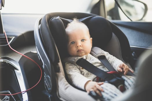 Cute little baby boy strapped into infant car seat in passenger compartment during car drive.