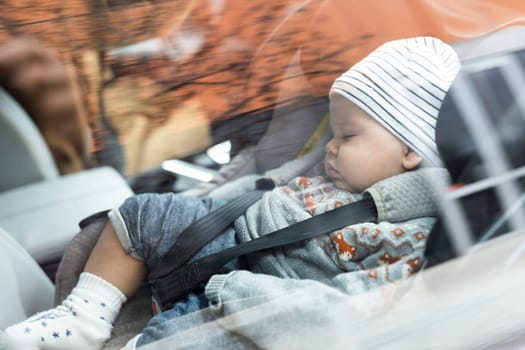 Cute little baby boy sleeping strapped into infant car seat in passenger compartment during car drive.