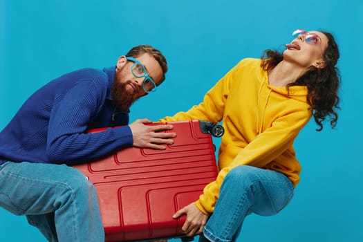 Woman and man smile suitcases in hand with yellow and red suitcase smile fun, on blue background, packing for a trip, family vacation trip.