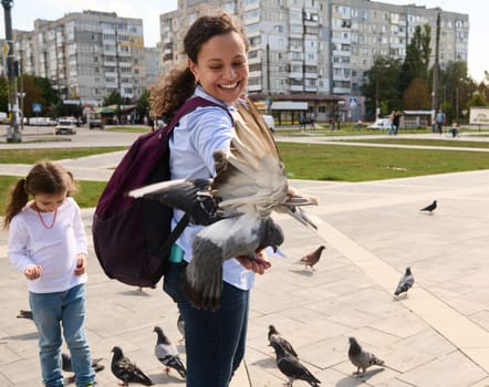 Smiling woman tourist expressing positive emotions while feeding rock pigeons and feral doves in the urban square