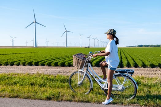 young woman electric green bike bicycle by windmill farm , windmills isolated on a beautiful summer