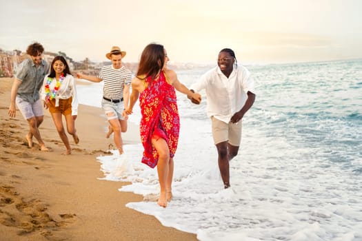Young multiracial happy, smiling group of friends running along seaside during vacation travel.