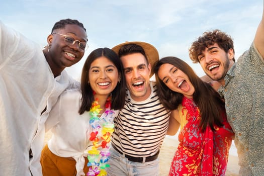 Happy, smiling group of multiracial friends relaxing at the beach having fun together looking at camera.