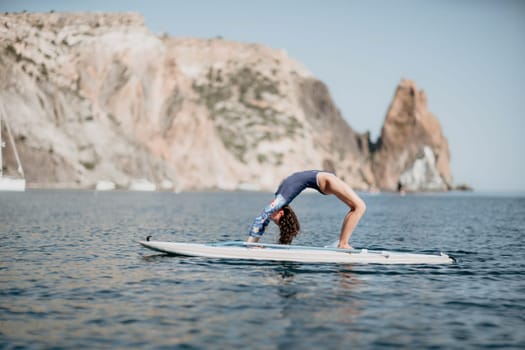 Woman sup yoga. Middle age sporty woman practising yoga pilates on paddle sup surfboard. Female stretching doing workout on sea water. Modern individual female hipster outdoor summer sport activity.