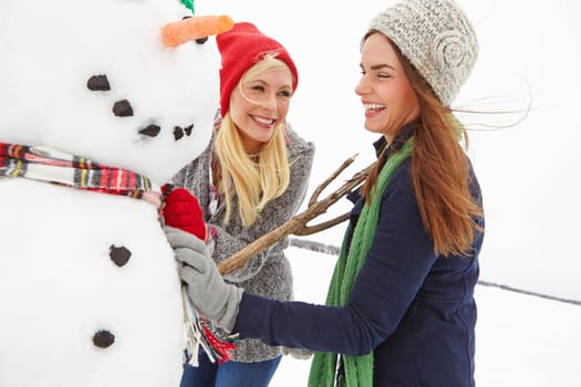 Glad that they finally finish their snowman. two beautiful young women building a snowman.