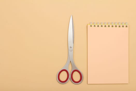 School supplies. Notebook and scissors on beige background.