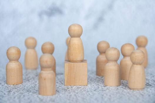 A wooden figure on top of wooden block representing a leader surrounded by other wooden figure. Leadership concept