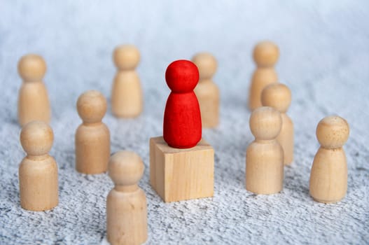 Red wooden figure on top of wooden block surrounded by other wooden figure. Leadership concept