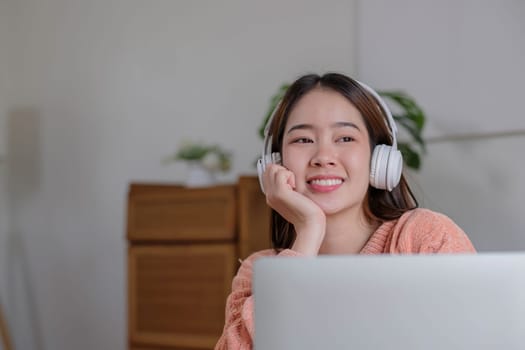 Pleased young woman in headphones with laptop listening to music while relaxing at home