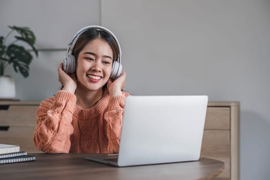 Pleased young woman in headphones with laptop listening to music while relaxing at home