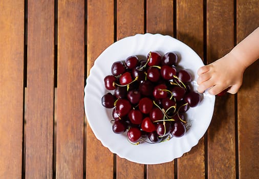 A white plate with many red cherrys on the old brown wooden background.