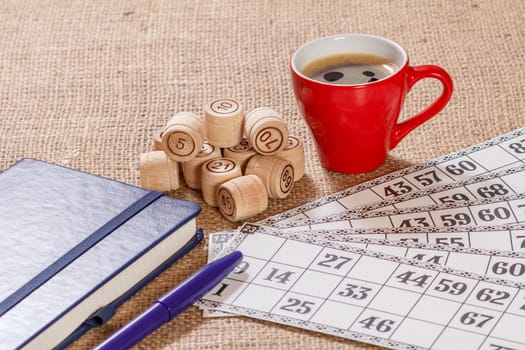 Board game lotto on sackcloth. Wooden lotto barrels and game cards with a cup of coffee and a notebook.