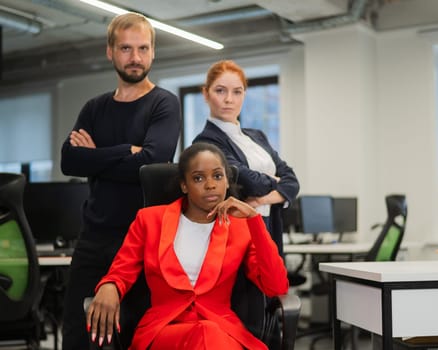 Caucasian red-haired woman, bearded Caucasian man stand behind a seated African American young woman in the office.