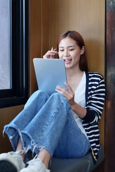 Portrait of a smiling Asian teenage girl using a tablet computer to study online via video conferencing