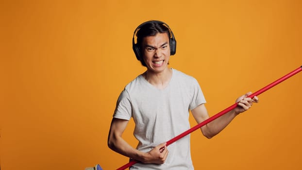 Asian carefree guy playing guitar with broom