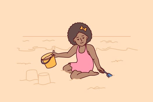 Little girl playing with sand sitting on beach building castle with bucket during summer holidays