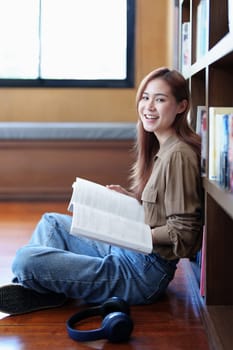 A portrait of a young Asian woman with a smiling face looking for a textbook in the library