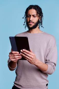 Confused arab man scrolling software app on digital tablet