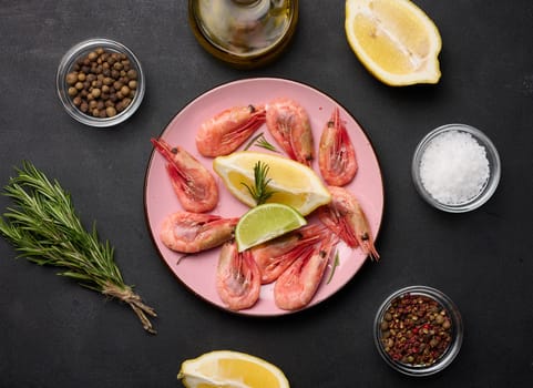 Boiled shrimp, lemon and lime slices, spices on a black table, top view