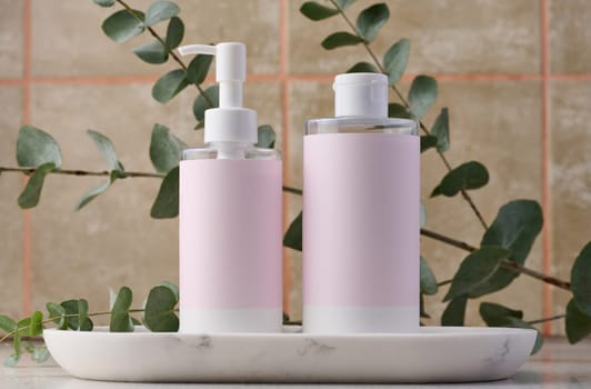 Two bottles for cosmetics with a pink paper label on a white background. Bottle for tonic, gel