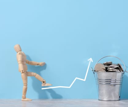 A wooden mannequin and coins in a miniature bucket on a blue background, a concept of high income
