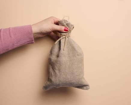A woman's hand holds a canvas bag on a beige background, the concept of a subsidy, help
