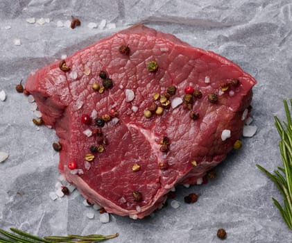 Raw piece of beef with spices lies on a white piece of parchment paper, top view