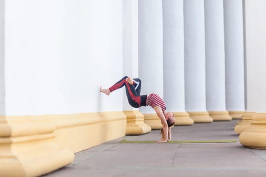 Slim attractive athletic sportswoman practicing yoga outdoor, doing wall-assisted handstand pose.