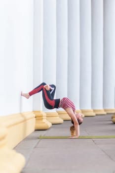 Sporty strong yogi young adult woman wearing sportswear doing wall-assisted handstand pose, yoga.