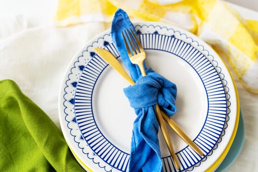 Serving design. Easter serving concept. Gold cutlery is tied with a blue napkin, on which the plates are on a green-yellow linen napkin. Minimalistic design.