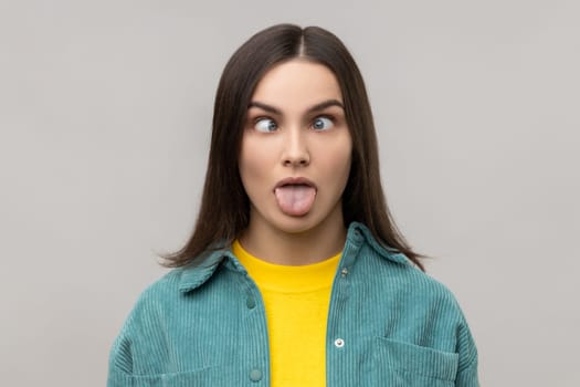 Woman sticking out tongue and looking at camera with crossed eyes, teasing with naughty expression.