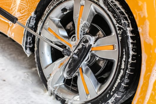 Yellow car wheel washed in self service carwash, brush cleaning aluminium rim disc covered in shampoo