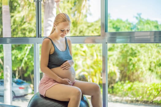 Pregnant woman exercising on fitball at home. Pregnant woman doing relax exercises with a fitness pilates ball. Against the background of the window