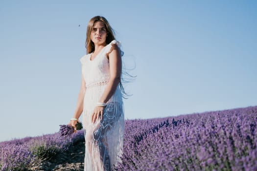 Woman lavender field. Happy carefree woman in a white dress walking in a lavender field and smelling a lavender bouquet on sunset. Ideal for warm and inspirational concepts in wanderlust and travel.