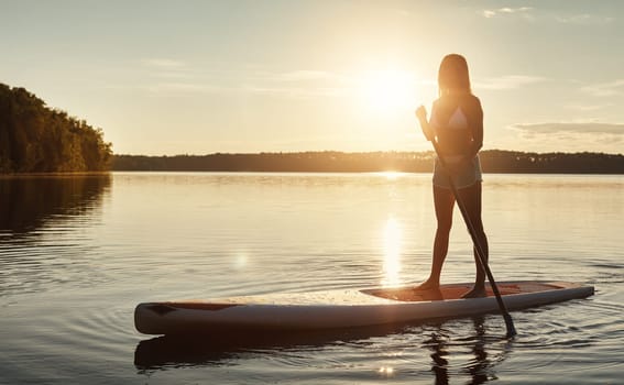This is her type of therapy. an attractive young woman paddle boarding on a lake.