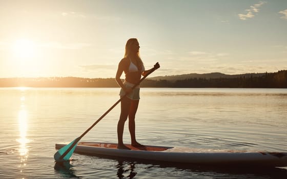 Seeking adventure. an attractive young woman paddle boarding on a lake.