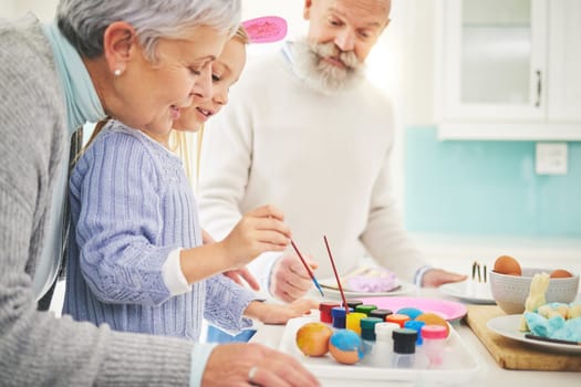 Easter, paint and a fun girl with her grandparents in their home for love, bonding or celebration together. Family, kitchen or egg with senior couple and grandchild in a house for creative painting.