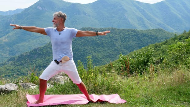 Older man senior practices yoga in the mountains, Virabhadrasana. Diabetic with medical device glucometer and urostoma sac
