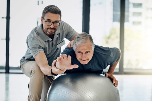 Recovery is within his reach. a caring physiotherapist helping his mature patient to use a yoga ball at a rehabilitation center.