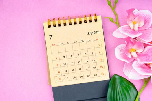 The July 2023 calendar desk and pink orchid on pink background.