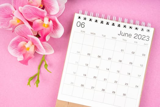 The June 2023 calendar desk and pink orchid on pink color background.