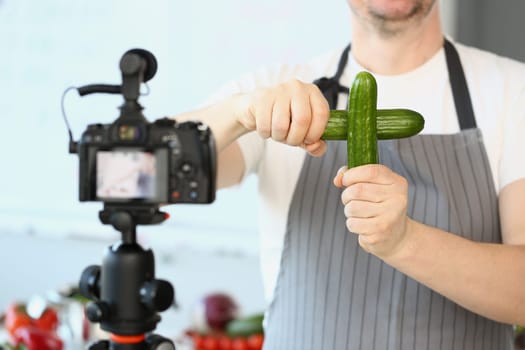 Male cook blog holding two cucumbers in front of camera