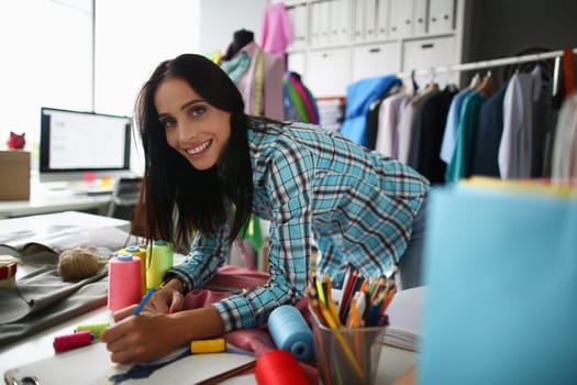 Smiling woman stylist designer seamstress draws clothes sketch