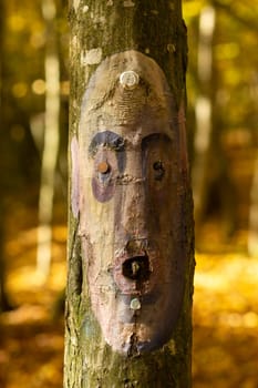A sad human face in the form of an icon is painted on the trunk of a tree