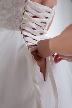 Woman's hands lace up corset on bride's dress