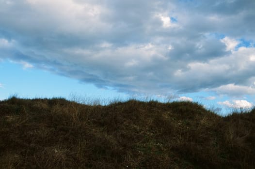 Grassy hill under cloudy blue sky