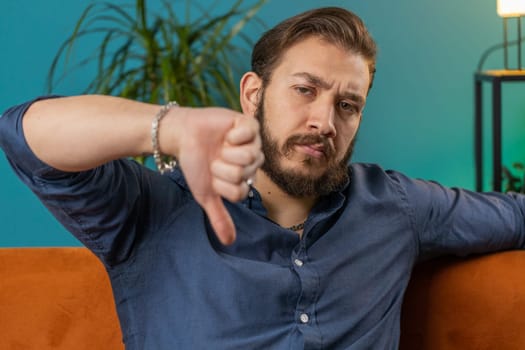 Upset lebanese man showing thumbs down, dislike bad work, disapproval, dissatisfied feedback at home