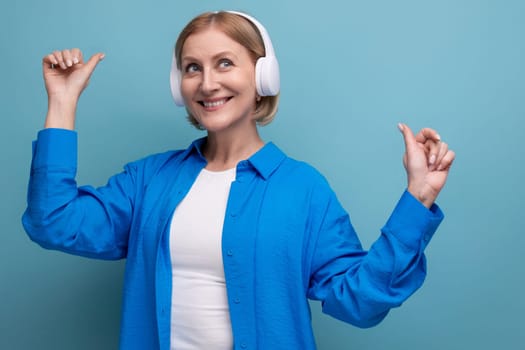 middle age business concept. 50s woman with headphones without wire dancing on blue background copy space
