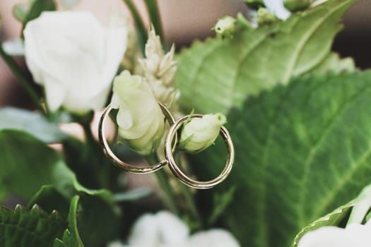 The wedding rings hang on a bridal bouquet