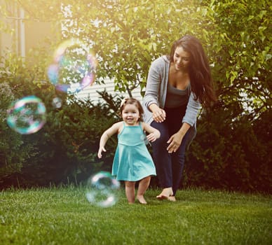 Weve got some bubbles to chase after, Mom. a mother and her adorable little daughter playing with bubbles outside.